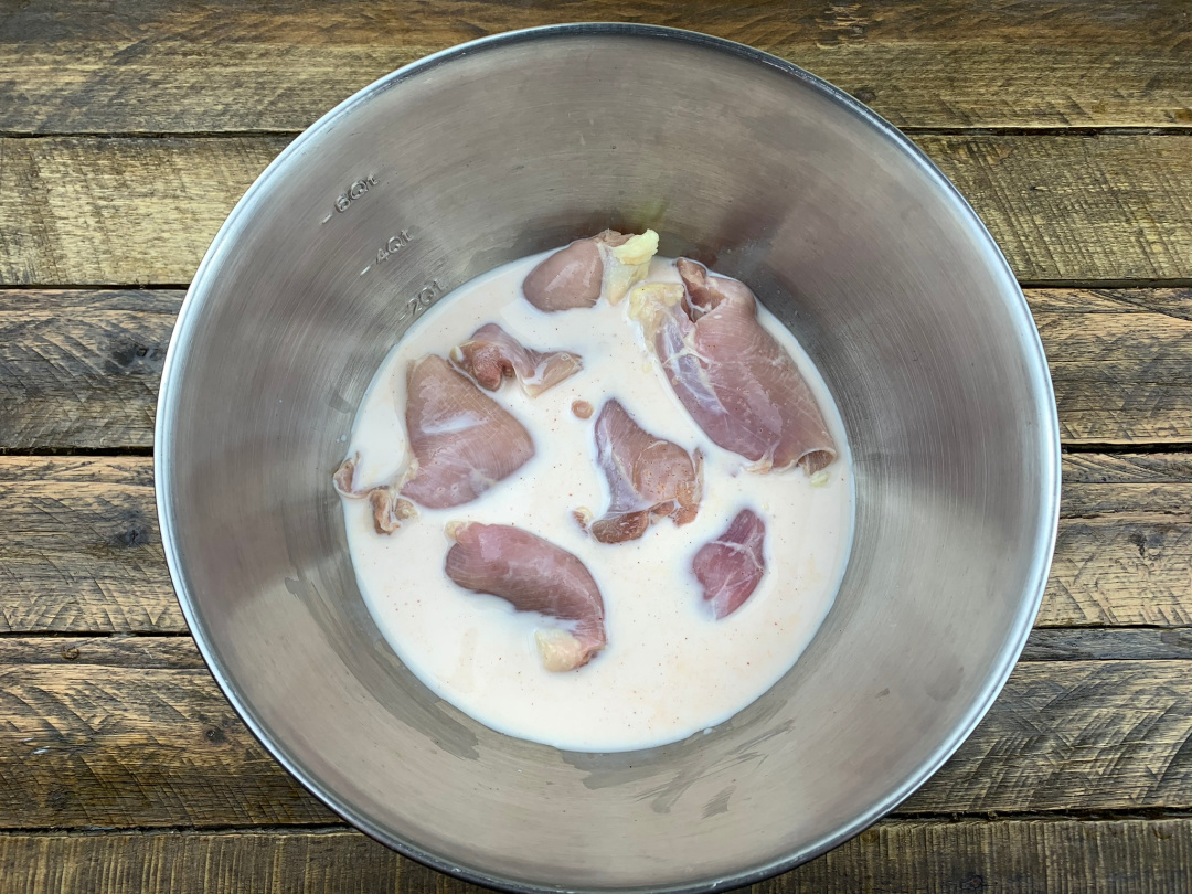 raw chicken thighs in a mixing bowl of buttermilk