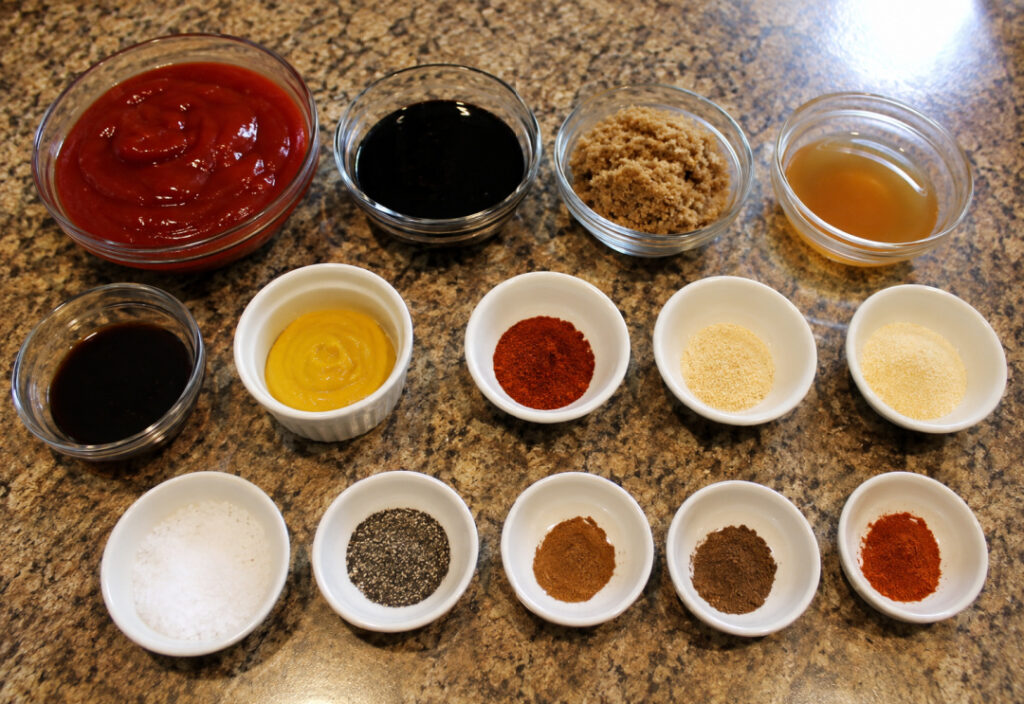 Ingredients for homemade BBQ sauce arranged in small bowls on a kitchen countertop, including ketchup, molasses, brown sugar, apple cider vinegar, Worcestershire sauce, mustard, and spices.