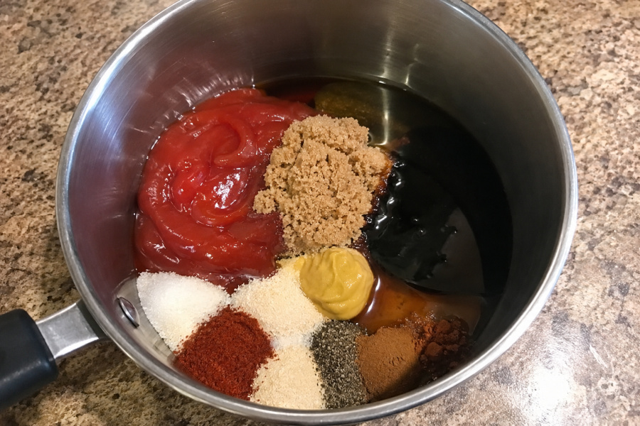 Ingredients for homemade BBQ sauce measured into a stainless steel saucepan, including ketchup, molasses, brown sugar, mustard, vinegar, Worcestershire sauce, and spices before cooking.