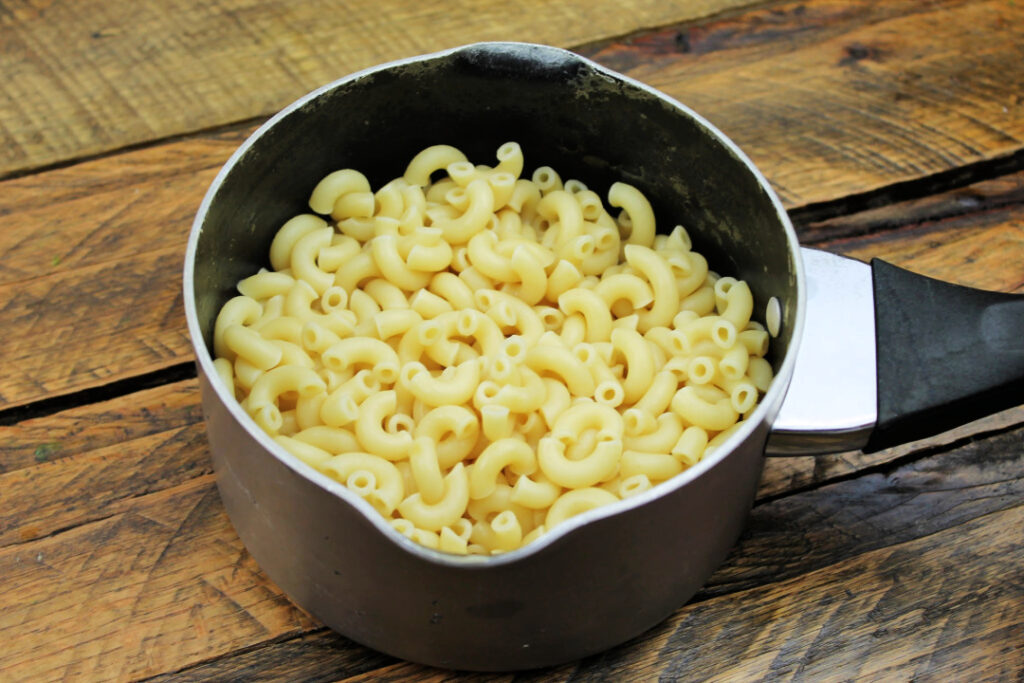 Cooked elbow macaroni in a saucepan, ready to be mixed with butter, milk, and cheese to make creamy homemade mac and cheese.