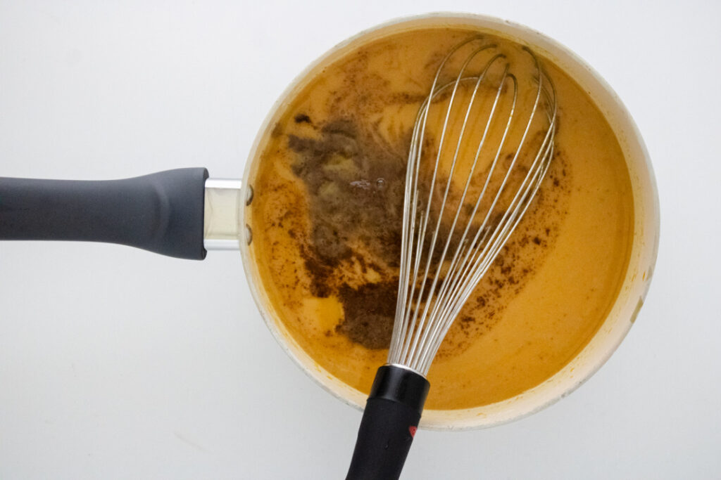 Pumpkin pie spice mixture being added to the homemade pumpkin spice syrup in a saucepan
