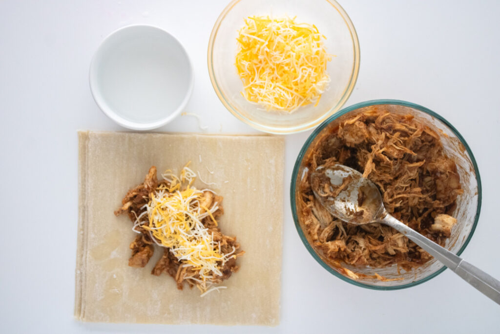 BBQ chicken and shredded cheese placed on egg roll wrappers before rolling.