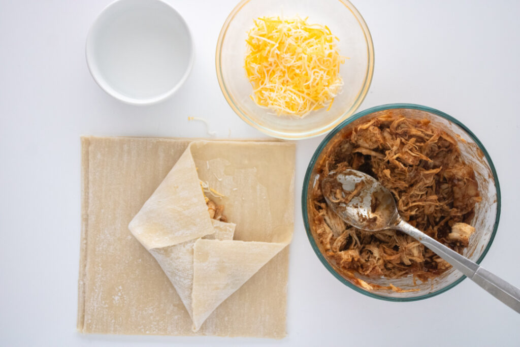 Folding the sides of an egg roll wrapper over the BBQ chicken and cheese filling.