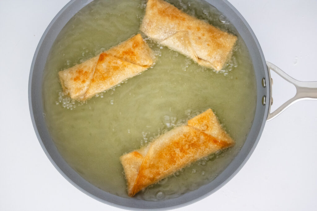 BBQ chicken egg rolls frying in vegetable oil until crispy and golden brown.