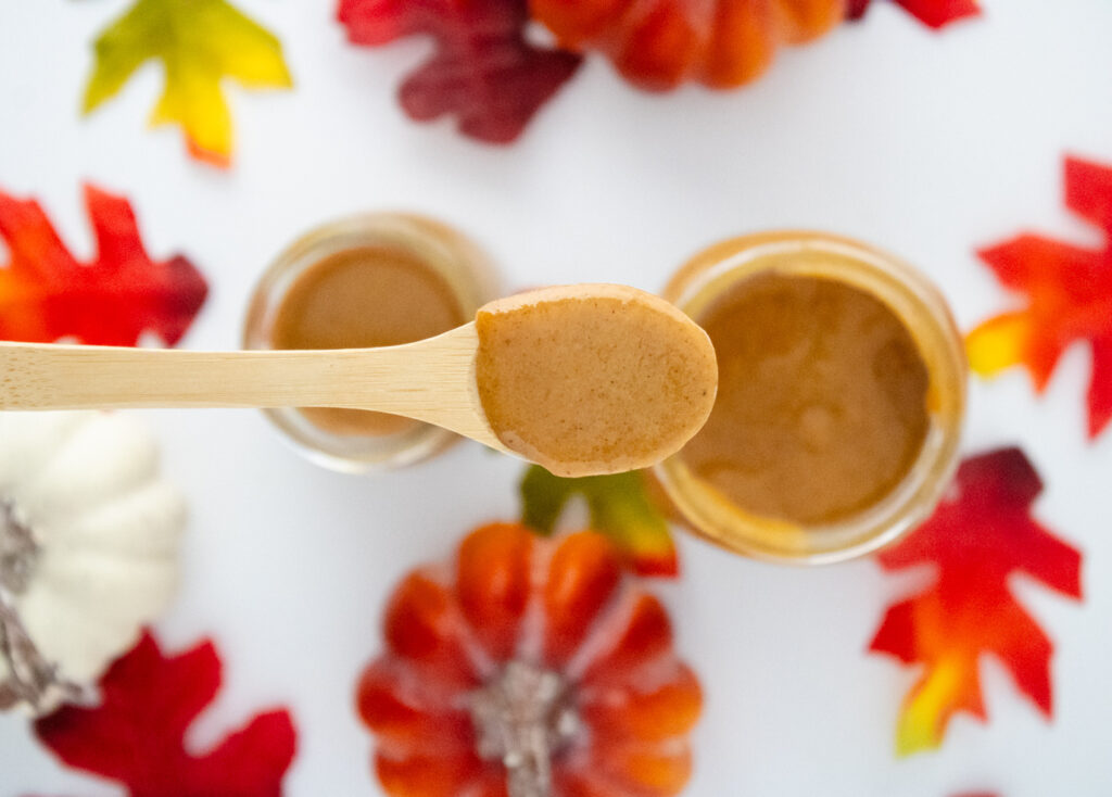 Spoonful of homemade pumpkin spice syrup with jars of syrup, pumpkins, and colorful fall leaves in the background.