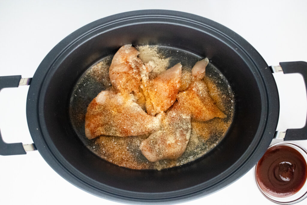 Chicken breasts coated with seasonings in the slow cooker for BBQ chicken egg rolls.