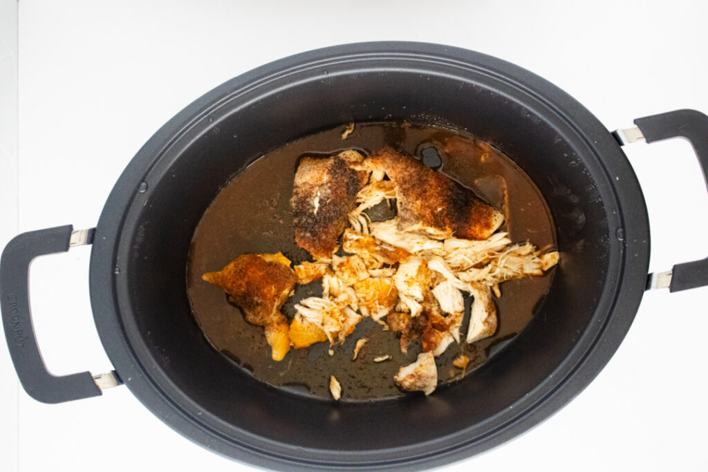 Cooked seasoned chicken partially shredded in the slow cooker for BBQ chicken egg rolls.