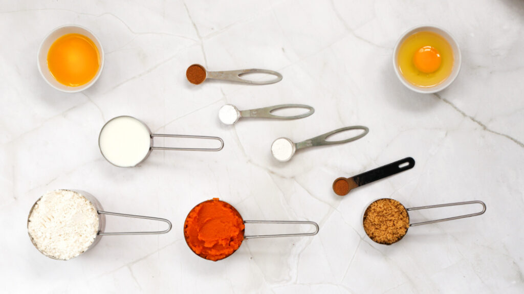 Ingredients for homemade pumpkin pancakes including pumpkin puree, flour, milk, egg, brown sugar, and spices