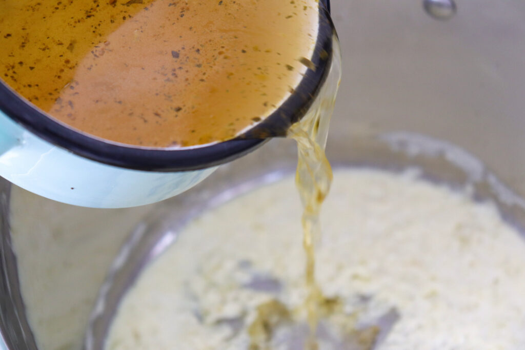 Pouring chicken broth into a Dutch oven while making homemade Broccoli Cheddar Soup.