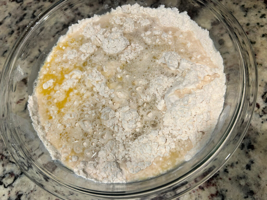 Warm water and melted butter added to the dry ingredients in a glass mixing bowl to begin making homemade basic white bread dough.