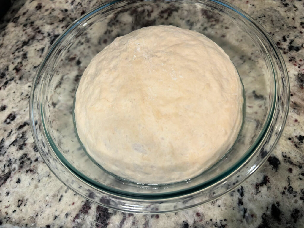 Homemade basic white bread dough after the first rise, doubled in size in a lightly greased glass bowl and ready to be shaped into a loaf.