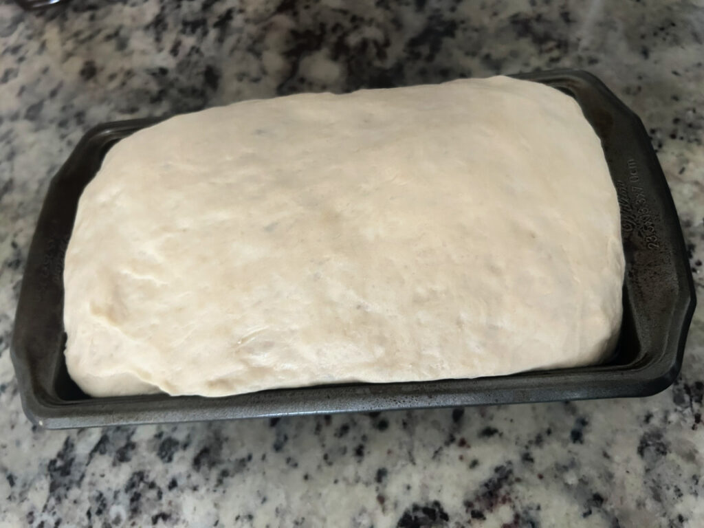Homemade basic white bread dough after the second rise, risen above the edge of the loaf pan and ready to bake.