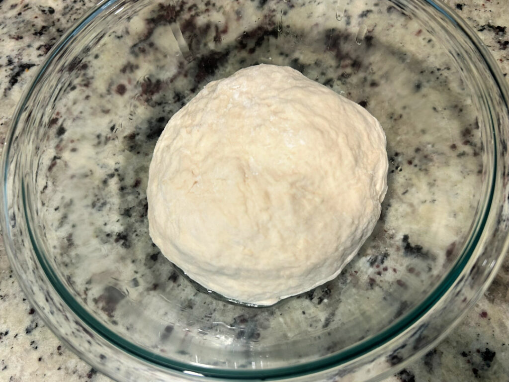 A smooth ball of homemade basic white bread dough placed in a lightly greased glass bowl, ready to rise until doubled in size.