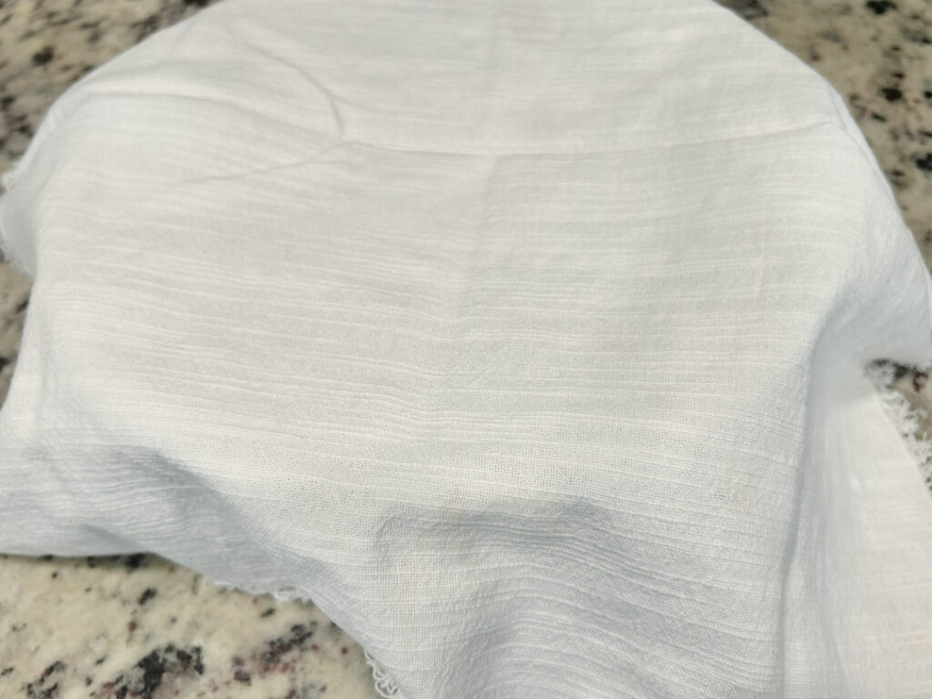 A bowl of homemade basic white bread dough covered with a clean kitchen towel while resting for the first rise.