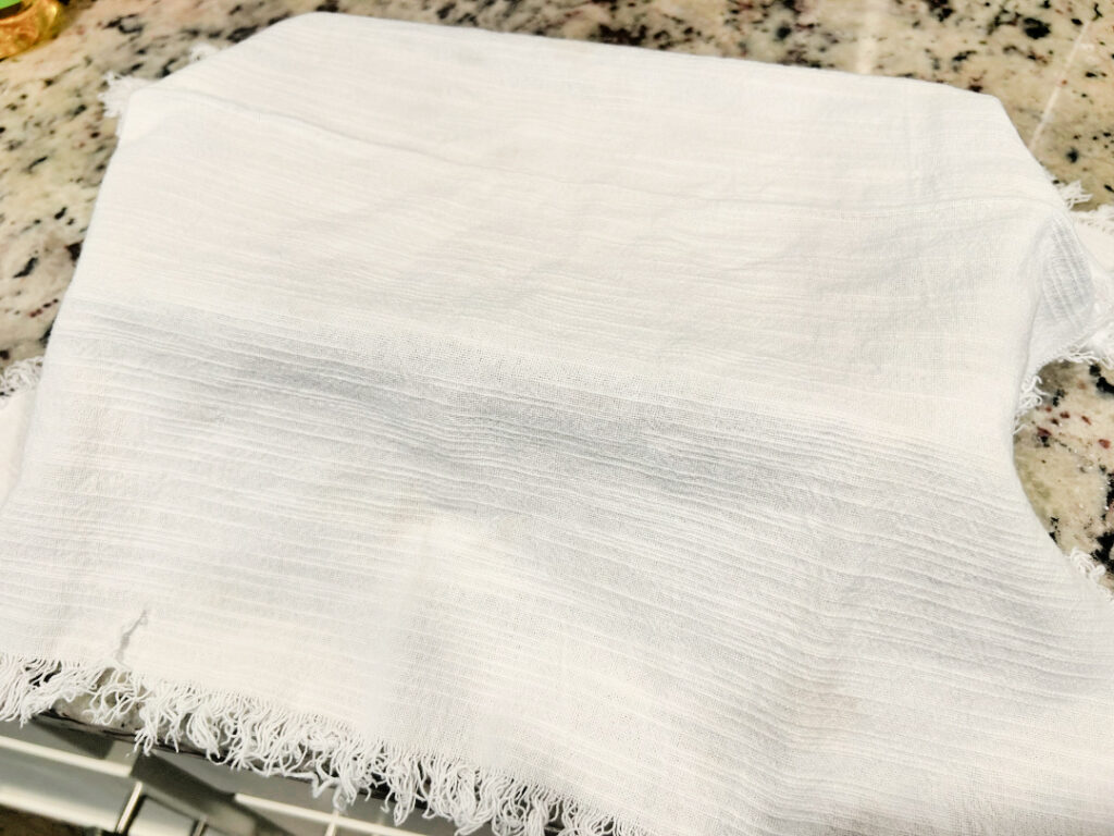 A loaf pan of homemade basic white bread dough covered with a clean kitchen towel while rising for the second time before baking