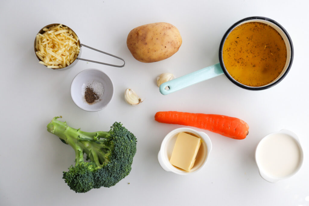 Ingredients for homemade Broccoli Cheddar Soup including fresh broccoli, shredded sharp cheddar cheese, potato, carrot, chicken broth, heavy cream, butter, garlic, salt, and black pepper.