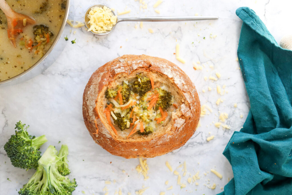 Overhead view of homemade Broccoli Cheddar Soup served in a crusty sourdough bread bowl with freshly shredded sharp cheddar cheese.