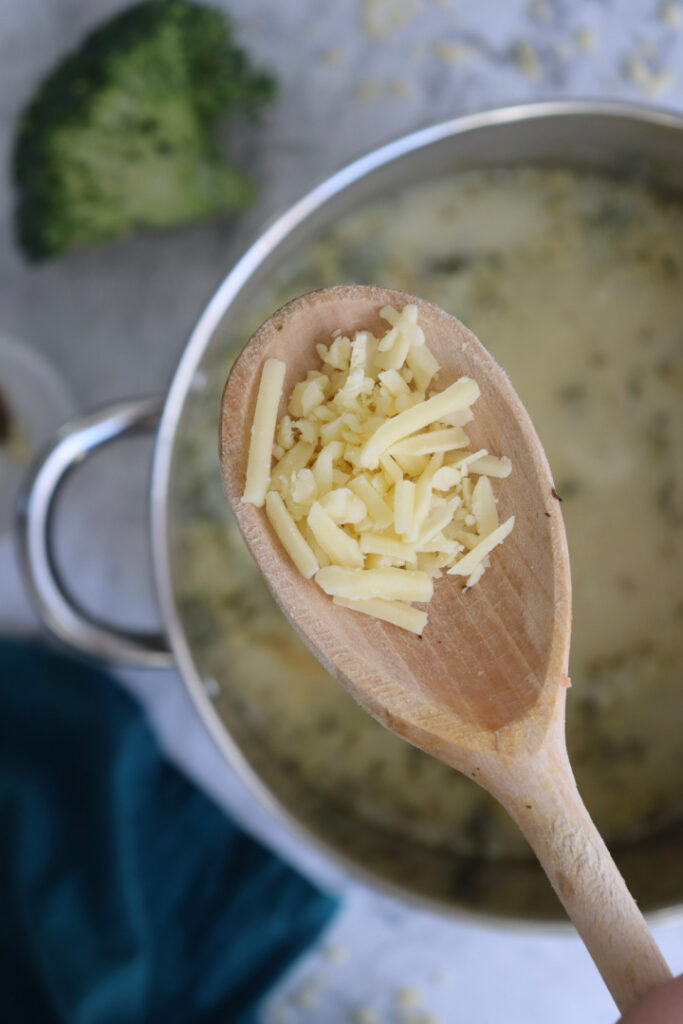Freshly shredded sharp cheddar cheese on a wooden spoon before being stirred into homemade Broccoli Cheddar Soup.