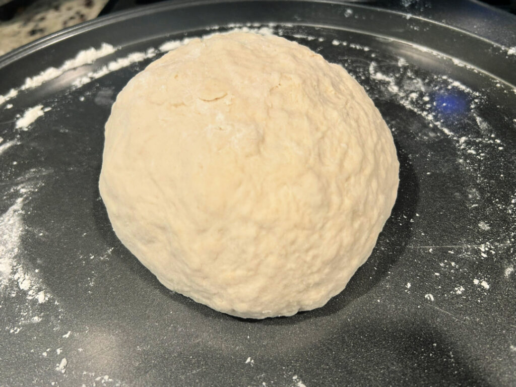 A smooth ball of homemade basic white bread dough after kneading, resting on a lightly floured surface and ready for the first rise.