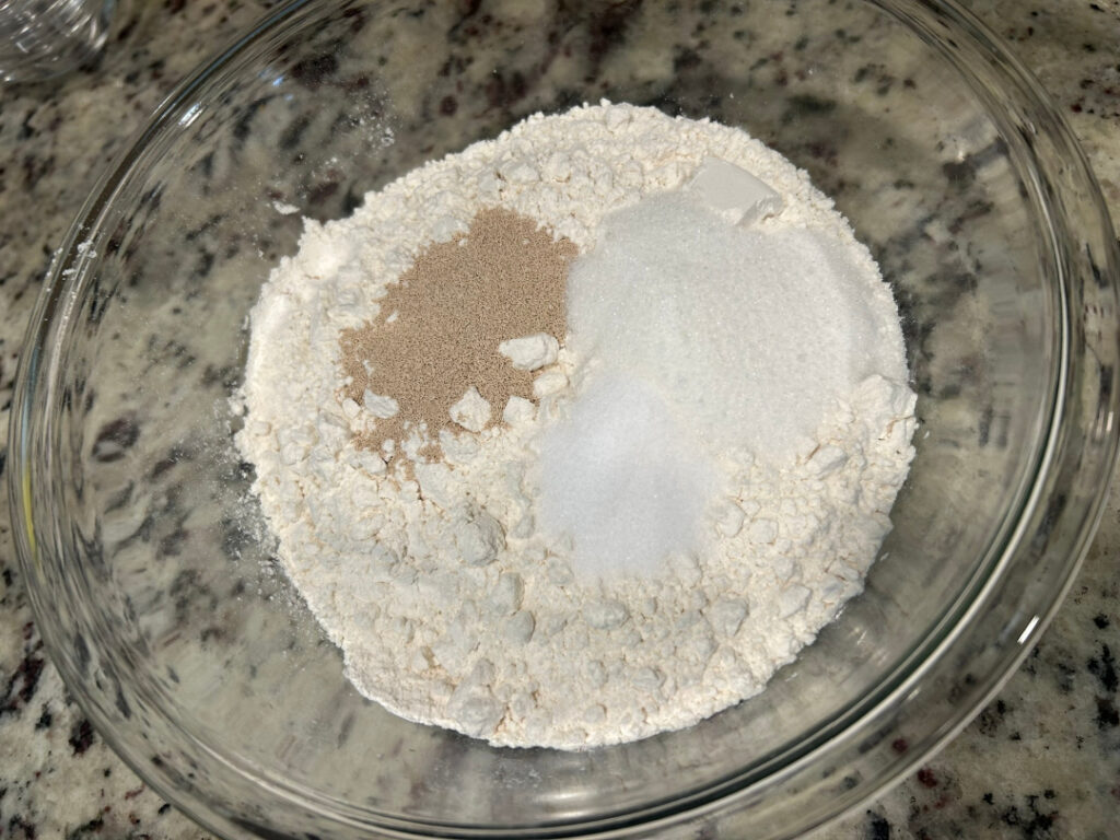 All-purpose flour, active dry yeast, sugar, and salt combined in a large glass mixing bowl before adding the wet ingredients for homemade basic white bread.