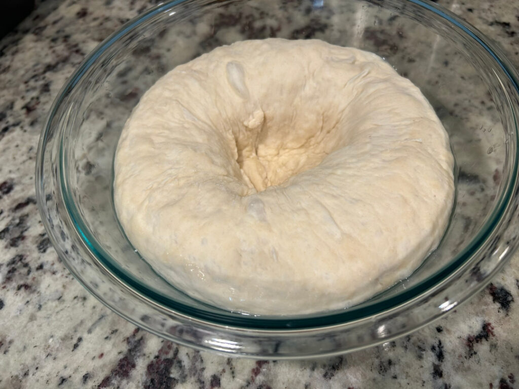 Homemade basic white bread dough after the first rise with the center pressed down to release air before shaping the loaf.