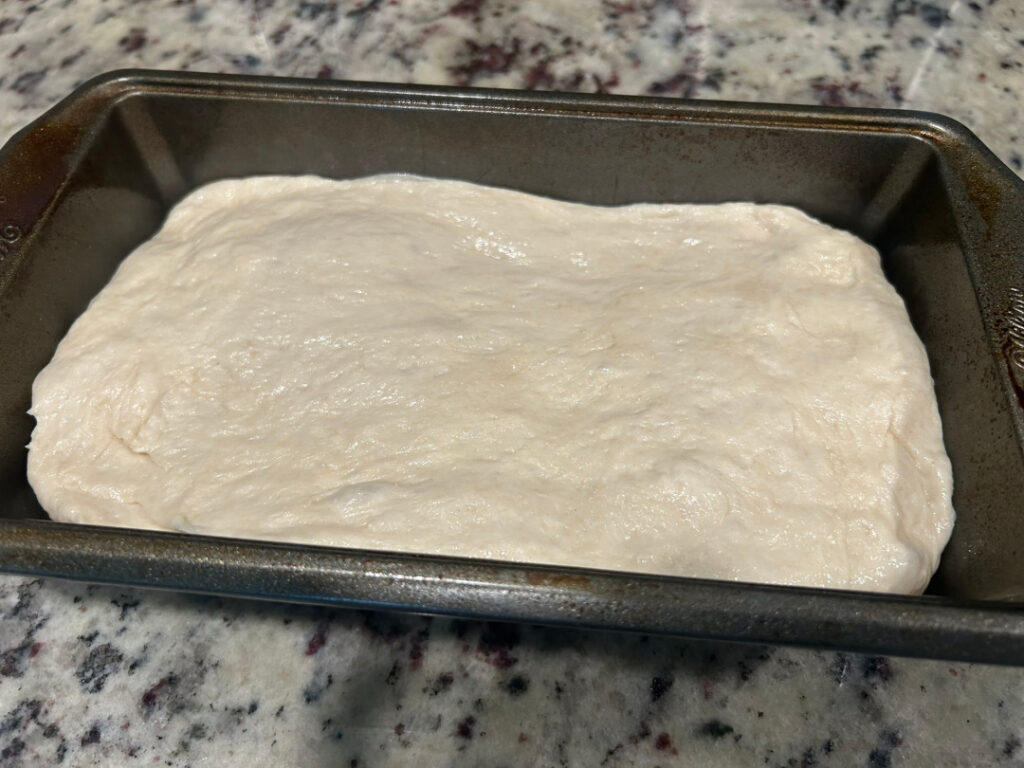 Homemade basic white bread dough shaped into a loaf and placed in a greased loaf pan before the second rise.