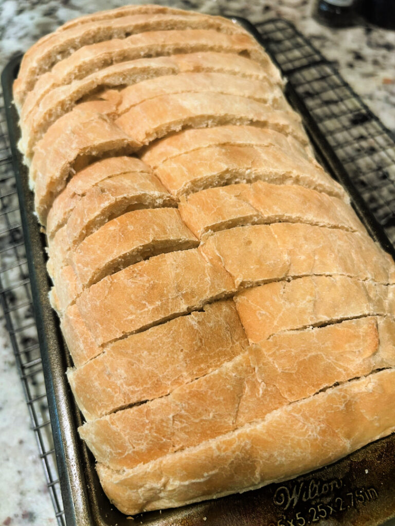 Freshly baked homemade basic white bread sliced into thick pieces, showing the soft interior and golden brown crust after cooling completely.
