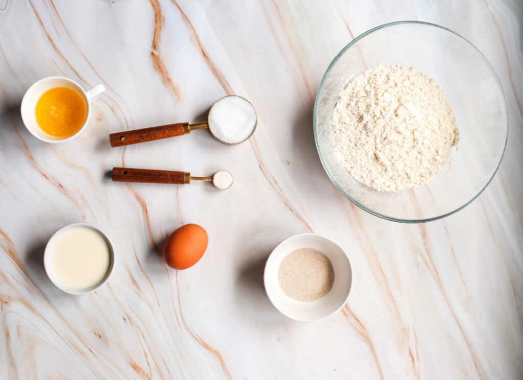 Flour, active dry yeast, sugar, salt, egg, melted butter, and milk measured for homemade apple pie cinnamon roll dough.