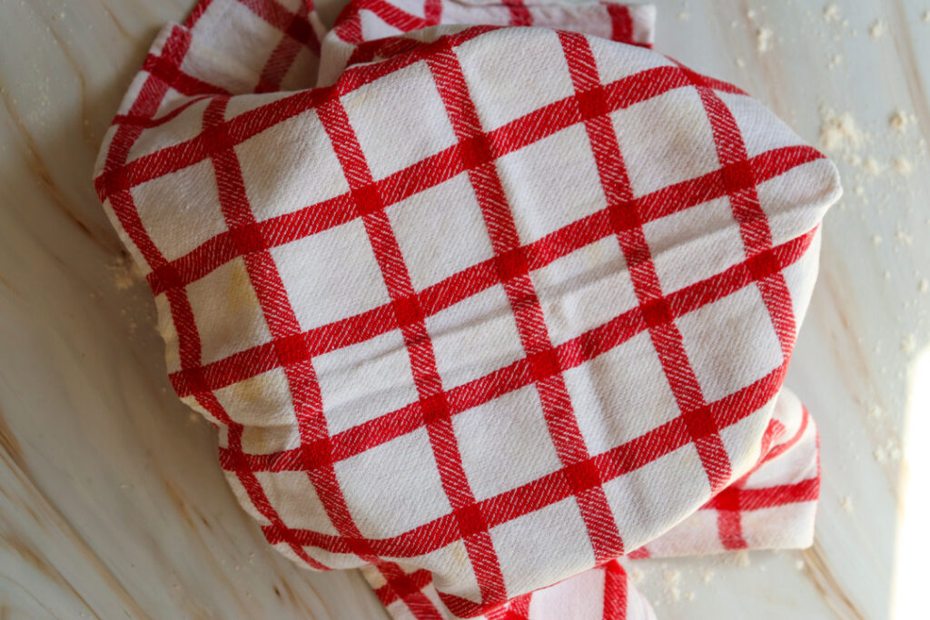 Cinnamon roll dough covered with a kitchen towel while it rises.