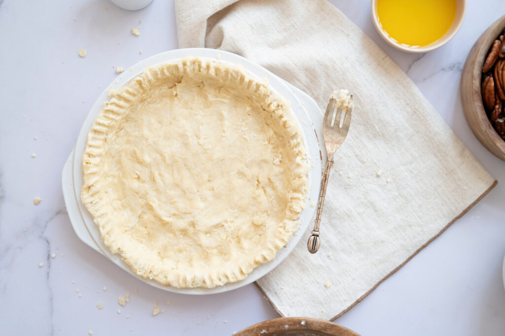 Homemade pie crust pressed into a pie dish with fork-crimped edges, ready for the classic pecan pie filling.
