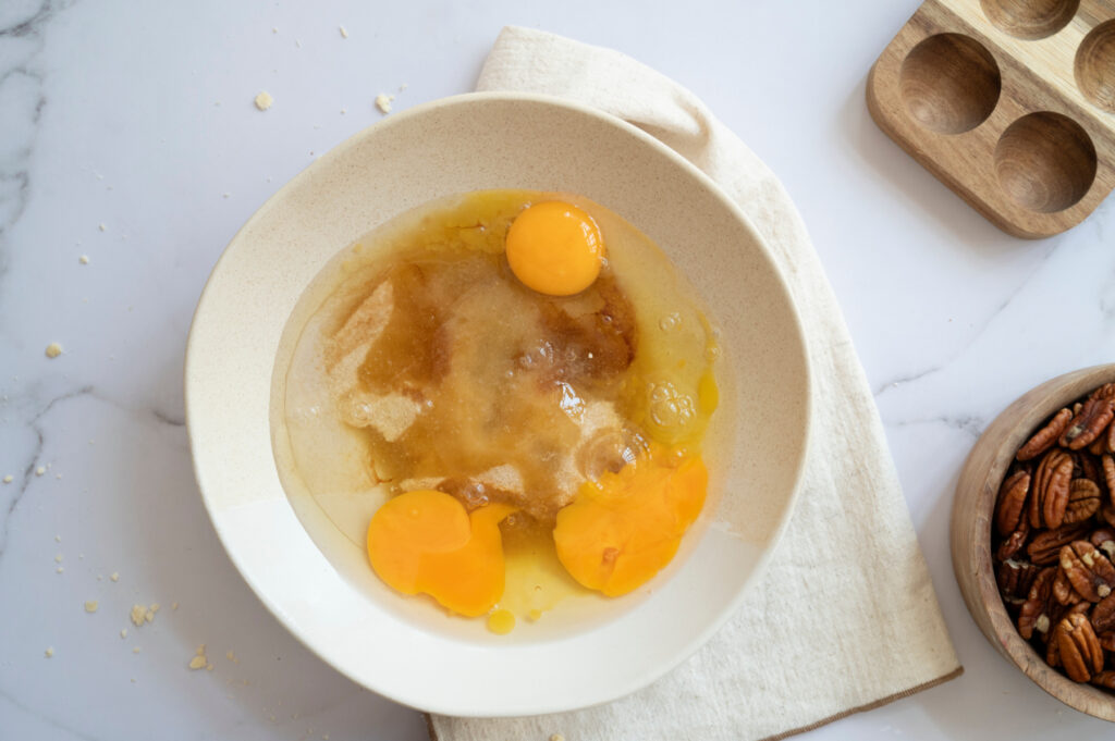 Eggs, brown sugar, corn syrup, melted butter, vanilla, and salt in a mixing bowl for classic pecan pie filling.
