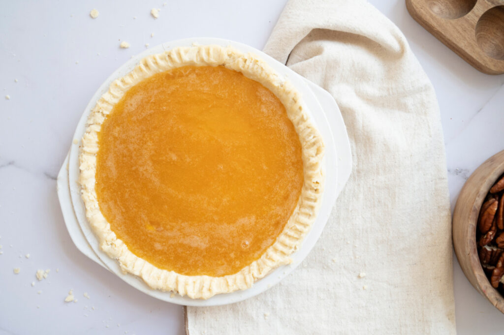 Classic pecan pie filling poured into an unbaked homemade pie crust with fork-crimped edges.