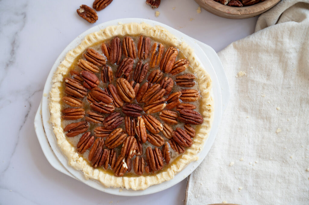 Pecan halves arranged in a circular pattern over the filling of an unbaked classic pecan pie, ready for the oven.