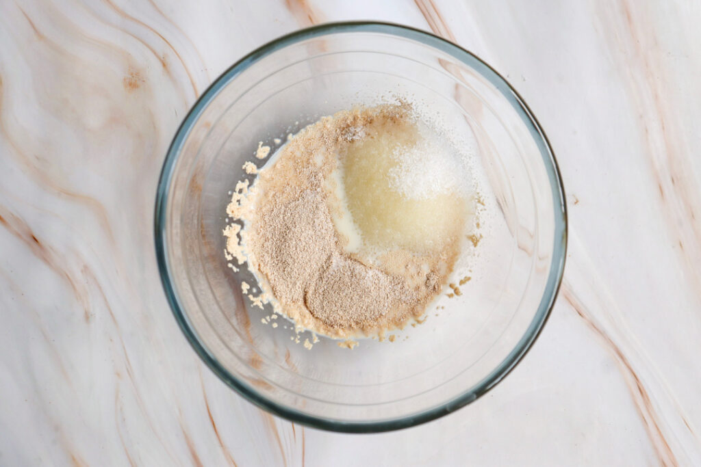 Active dry yeast, sugar, and warm milk in a glass bowl for homemade apple pie cinnamon roll dough.