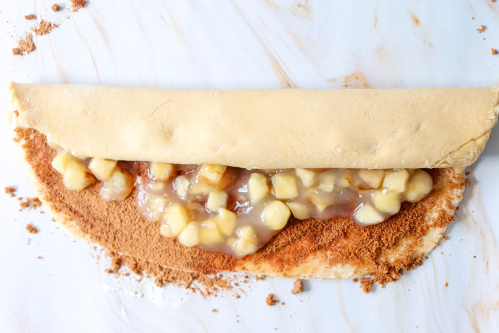 Apple and cinnamon-filled dough being rolled into a log before slicing into individual cinnamon rolls.