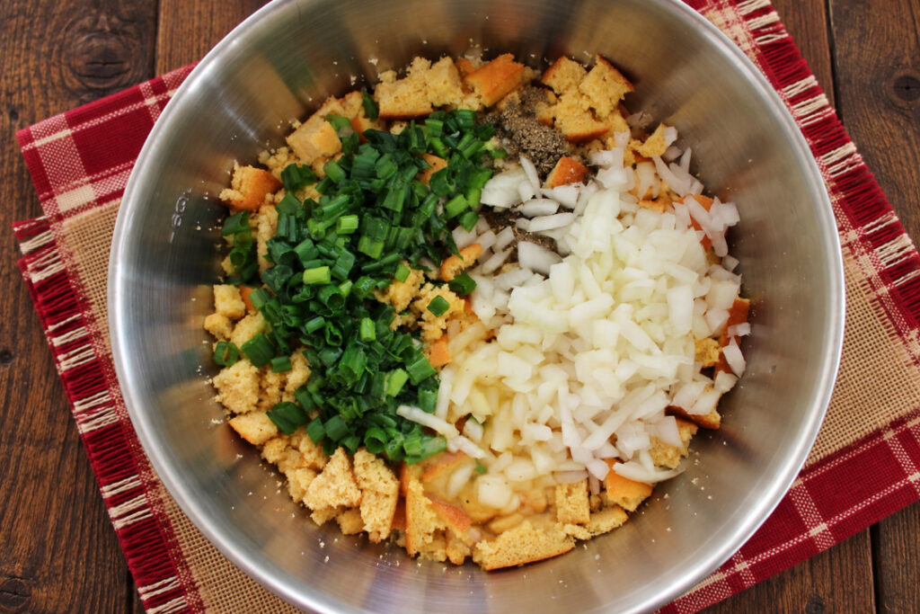 Crumbled bread with chopped onions, green onions, and seasonings in a mixing bowl for Southern cornbread dressing.