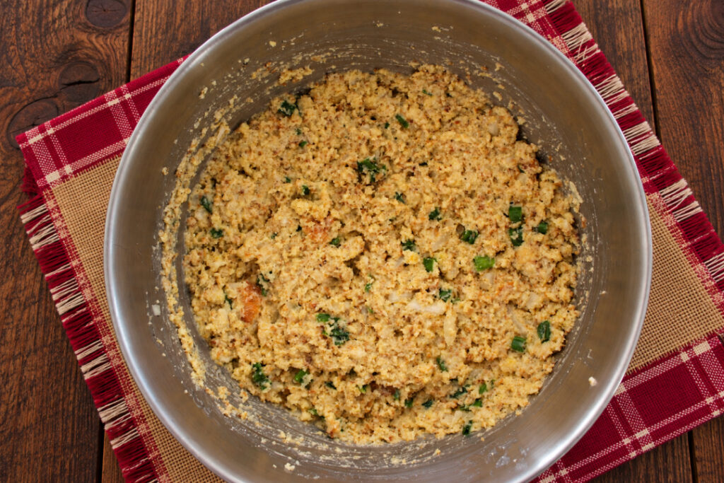 Southern cornbread dressing mixture with onions, green onions, sage, eggs, butter, and chicken broth combined in a mixing bowl.