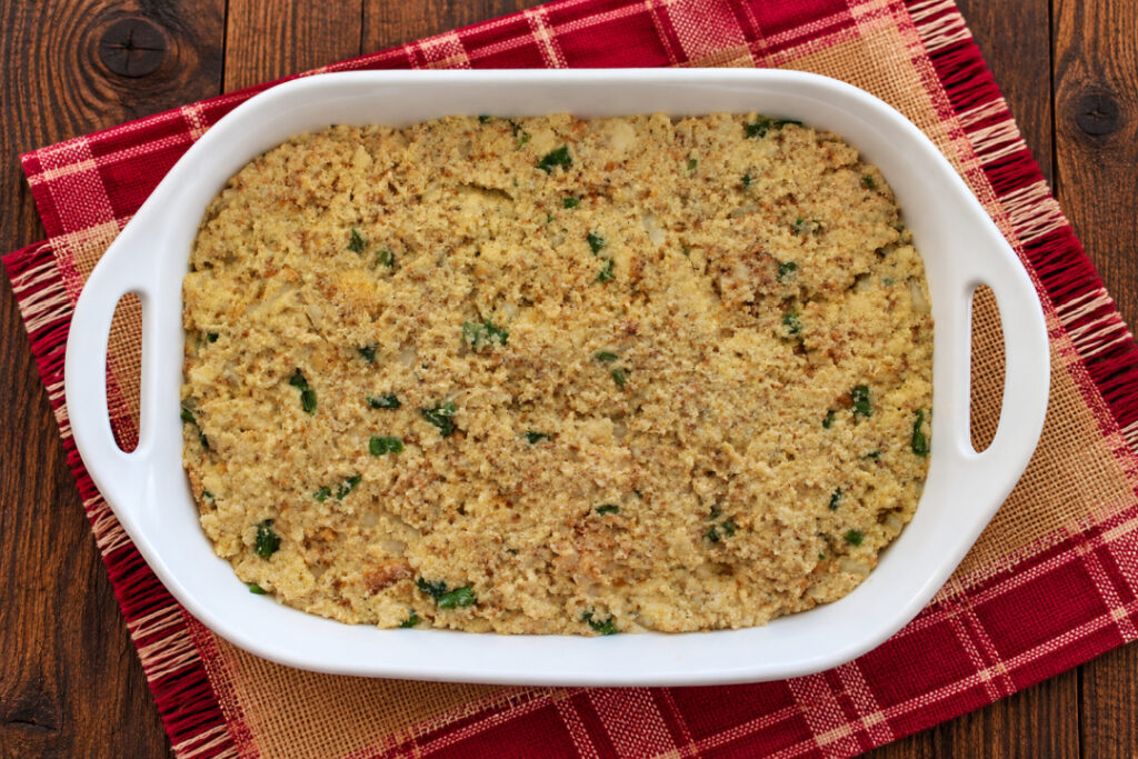 Unbaked Southern cornbread dressing spread in a white casserole dish and ready to go into the oven.