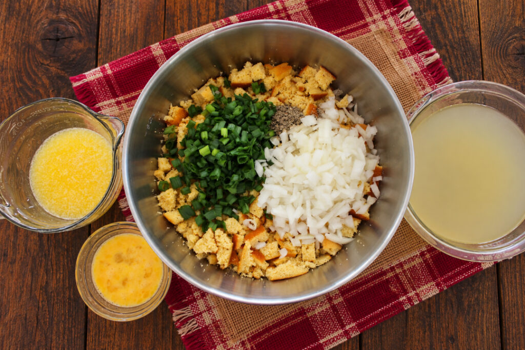 Cornbread dressing ingredients with chopped onions and green onions, melted butter, beaten eggs, and chicken broth ready to mix.