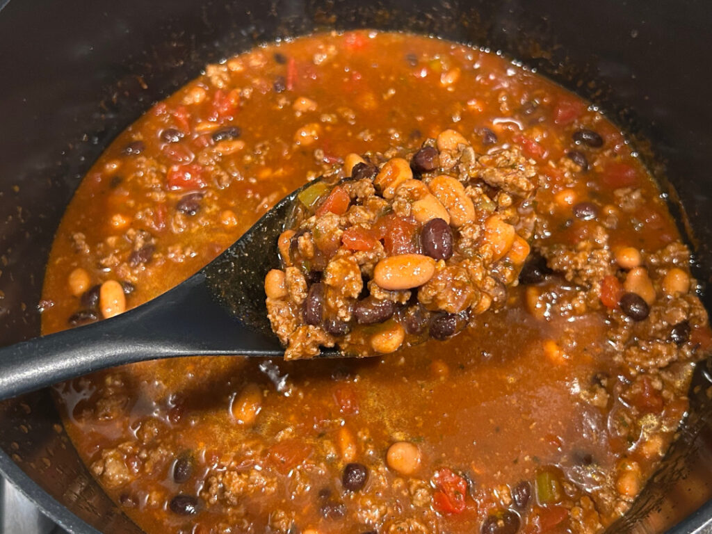 Spoonful of beef and bean chili with ground beef, pinto beans, black beans, and diced tomatoes.