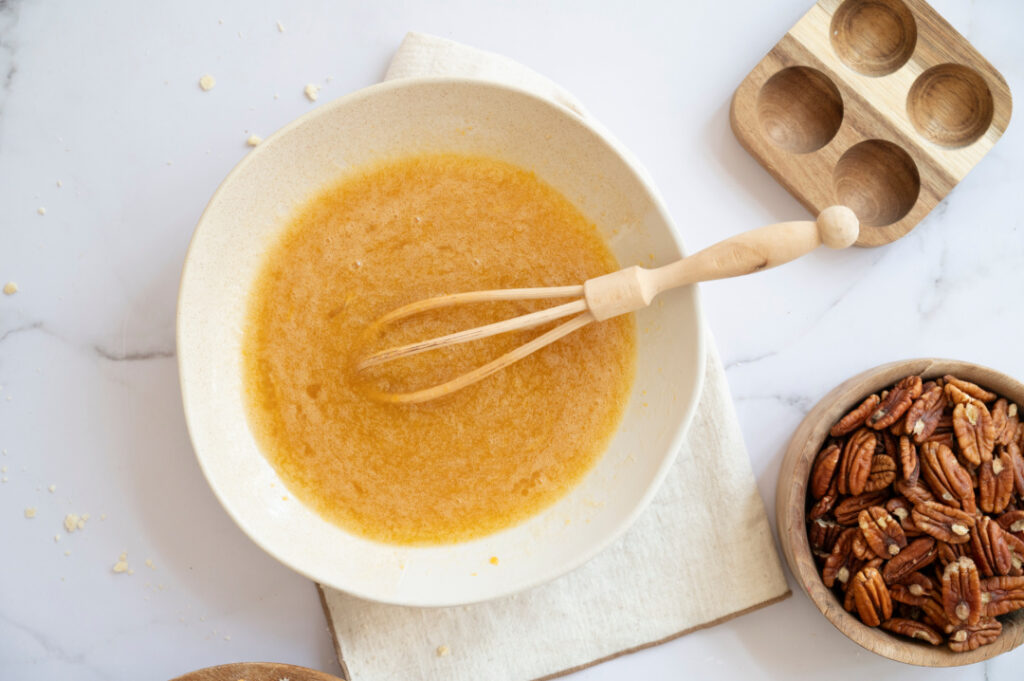 Classic pecan pie filling whisked together in a mixing bowl with pecans nearby, ready to pour into the pie crust.